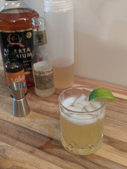 Features the stinger, a cross between a Moscow Mule and a Whiskey Sour. The drink is filled with ice and uses a lime for garnish. The drink uses Token Bitters Strathcona Orange Bitters and Alberta Premium Whiskey.