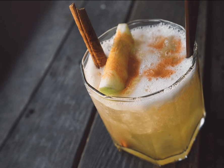 Apple Cider Old Fashioned, garnished with an apple slice, cinnamon stick, and powdered cinnamon.