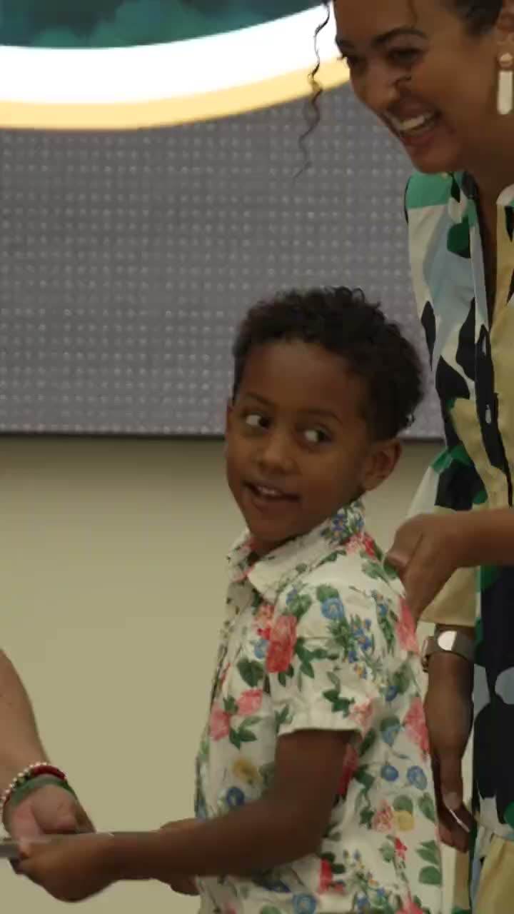 Cash, smiling back over his shoulder on stage at his child care graduation, his mom Jessica beside him