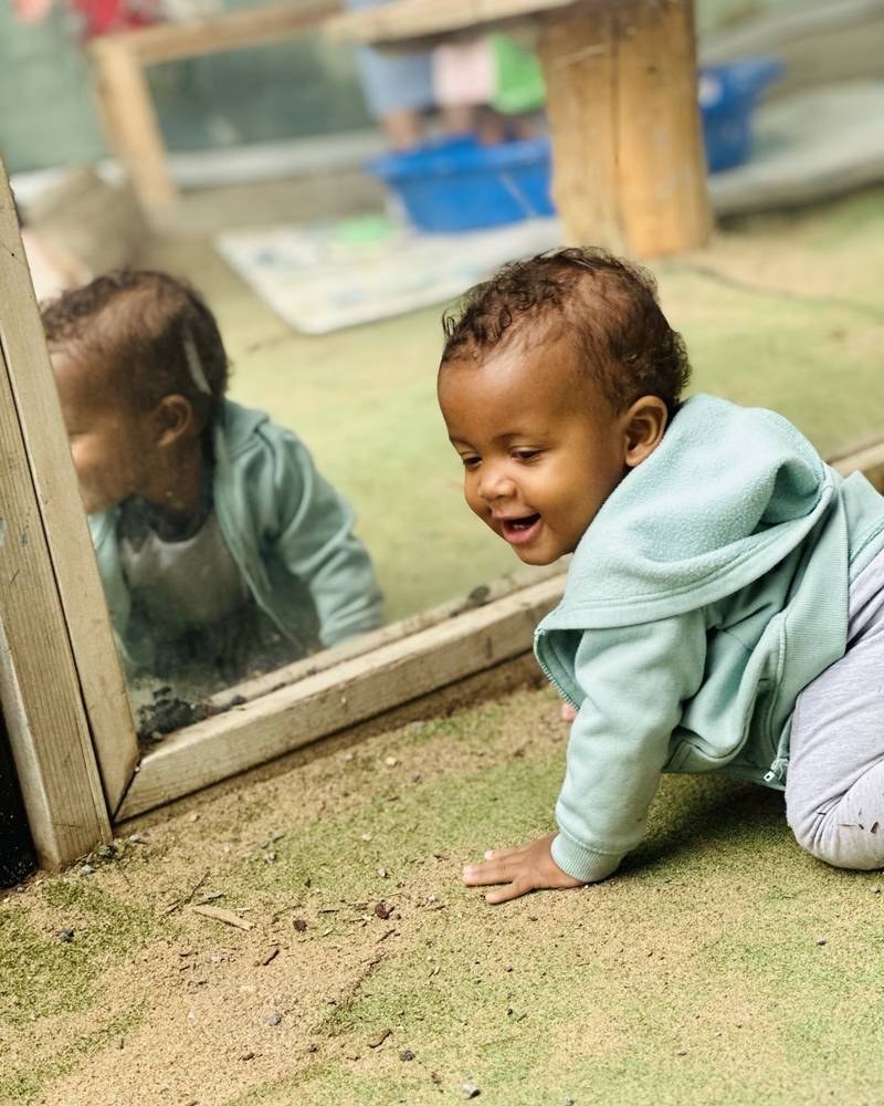The same baby crawling up to a low mirror and grinning at his reflection