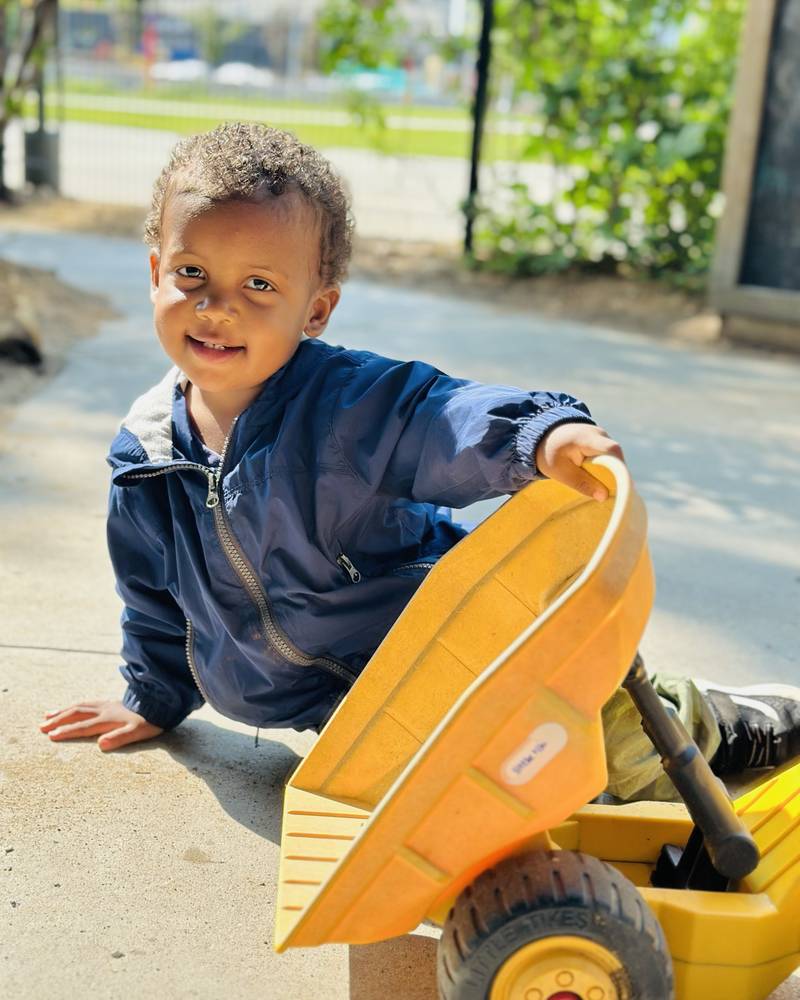 A toddler kneeling beside a big yellow toy dump truck