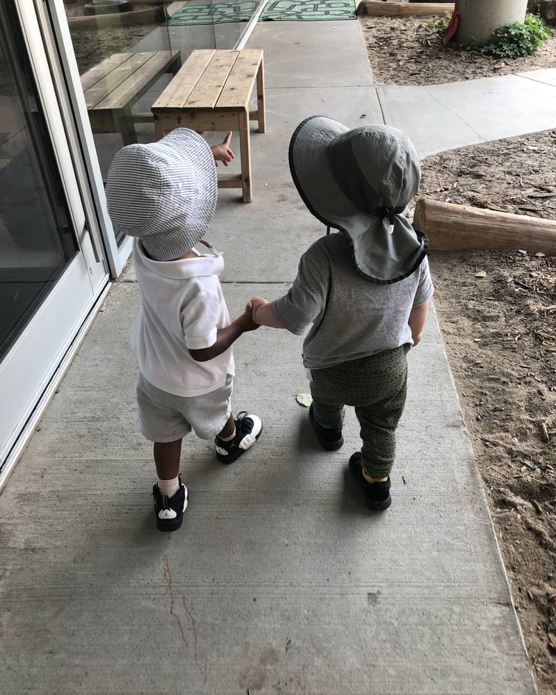 Two toddlers in sun hats walking away down a path, holding hands