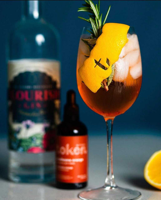 Strathcona Spritz cocktail, garnished with an orange twist and sprig of rosemary. Background features gin and orange bitters.