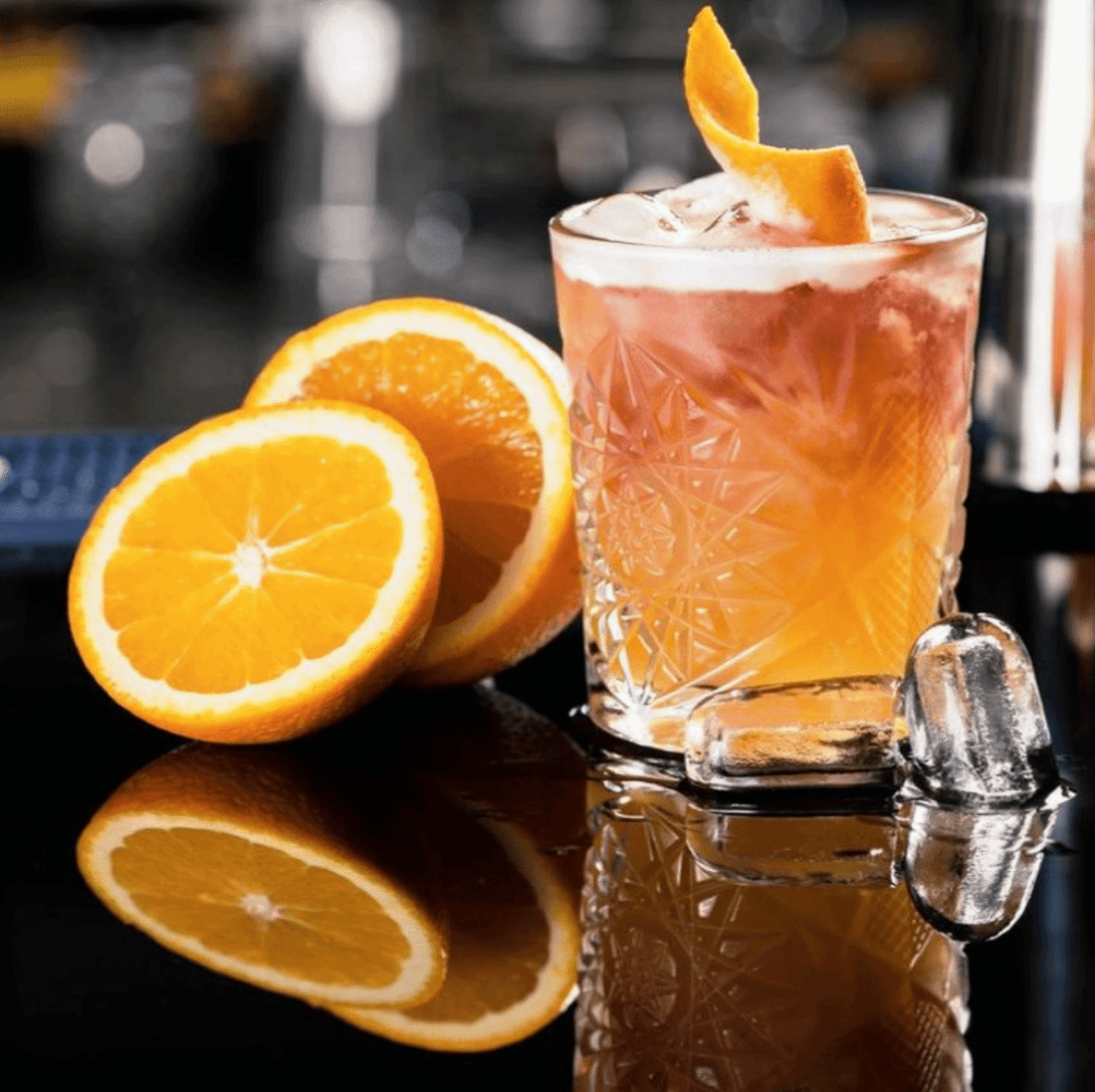 Pomegranate Orange cocktail, garnished with an orange twist. Cocktail features a colour change from orange to red