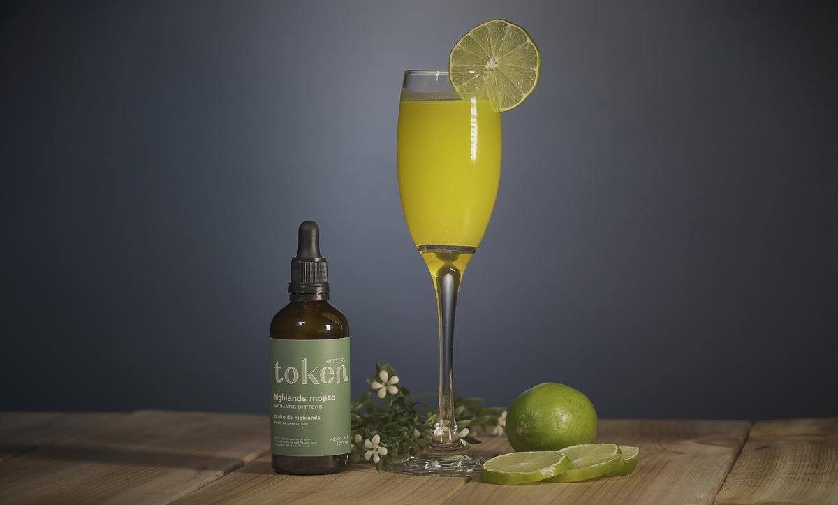 Key Limeade cocktail with a bottle of Token’s Highlands Mojito bitters and fresh lime slices 