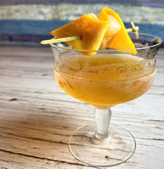 Orange cocktail garnished with an orange twist, served in a cocktail glass.