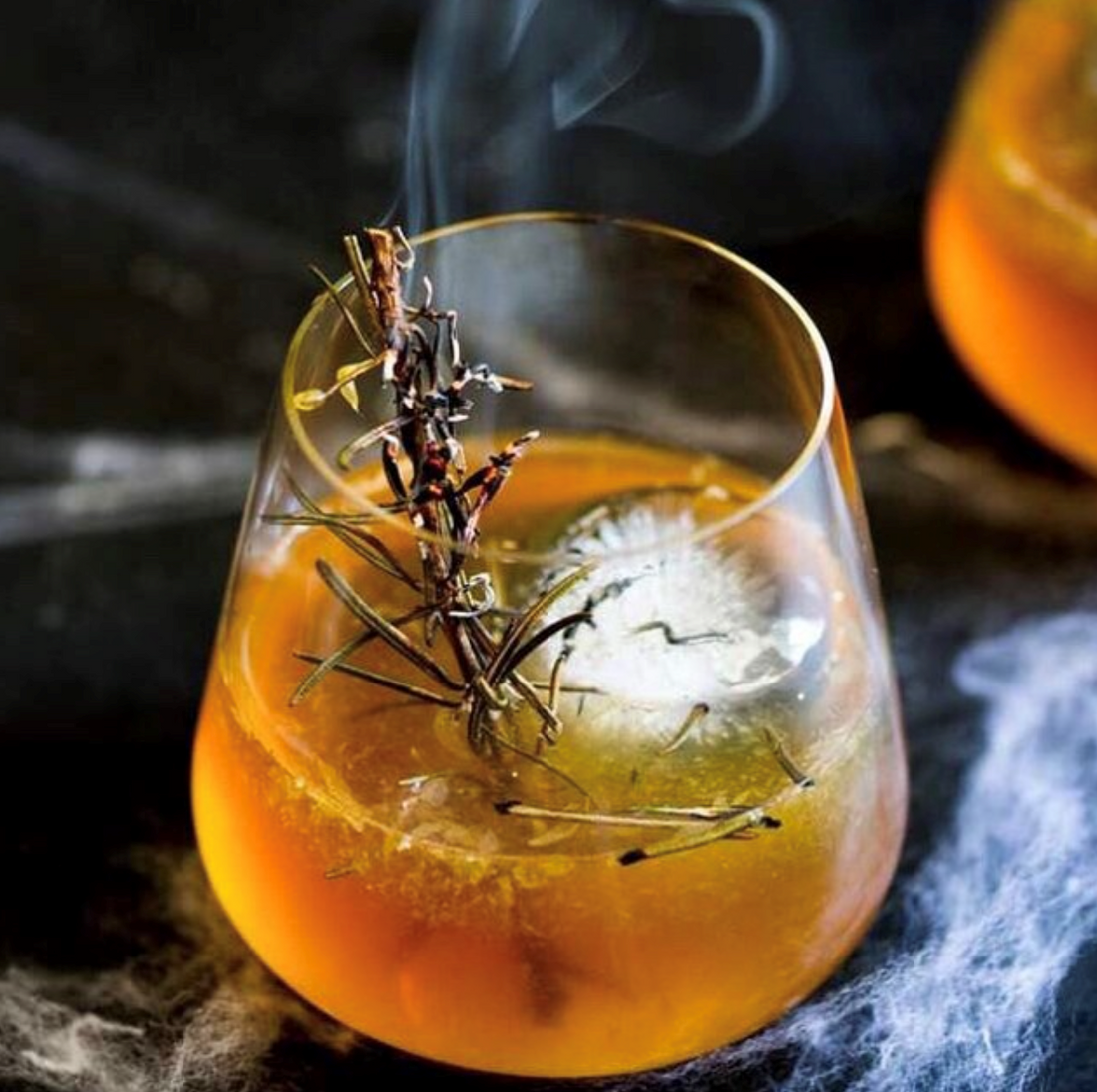 Orange cocktail garnished with a sprig of rosemary. Made with Bourbon, oranges, rosemary, and Token's Strathcona Orange Bitters.