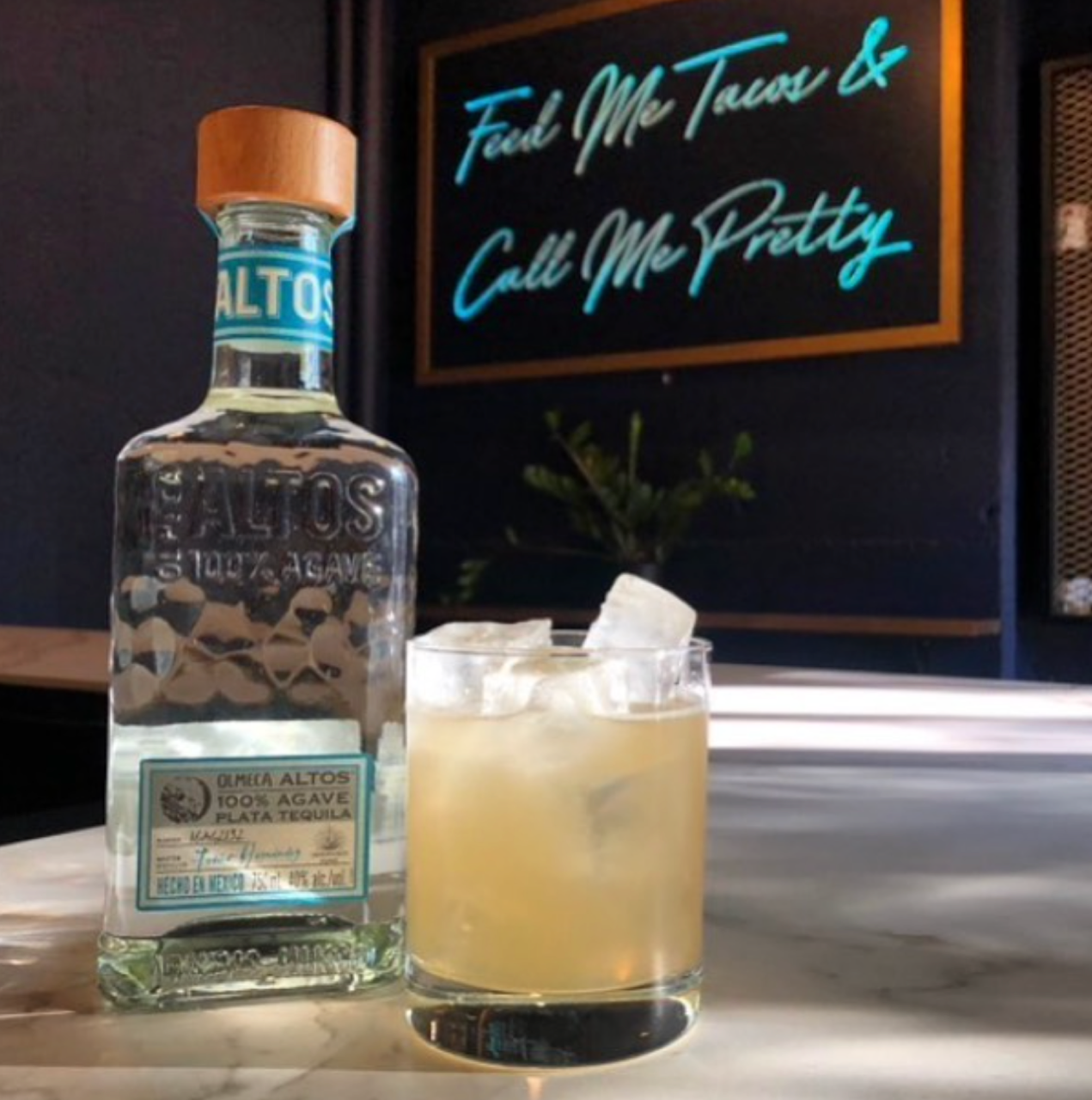 Margarita served over ice in a rocks glass. Features a bottle of Altos Plata tequila.