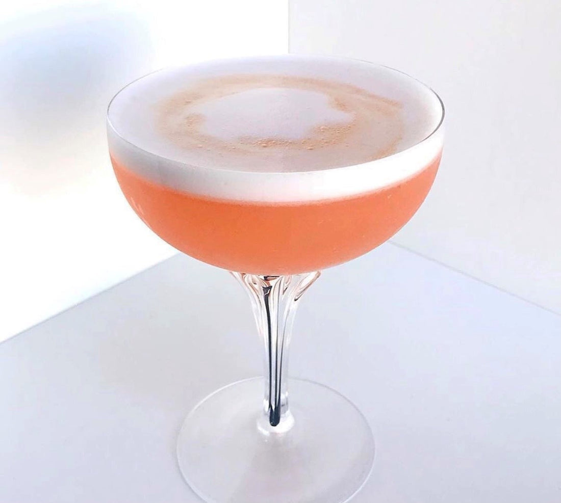 A salmon coloured cocktail featuring rum, fruits, and an egg white.
