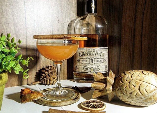 Orange Daiquiri served in a coupe glass, garnished with cinnamon and lemon. Features rum and assorted decorations in the background.