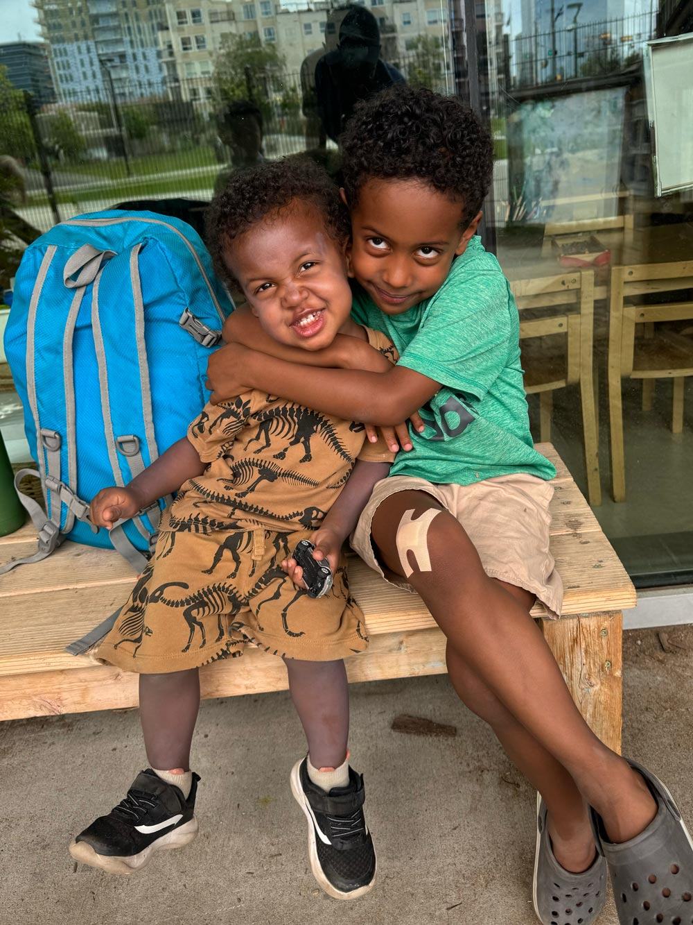 Cash hugging his little brother Roman on a wooden bench outside their child care centre, both grinning